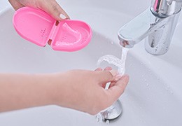 Person rinsing clear aligners under bathroom faucet